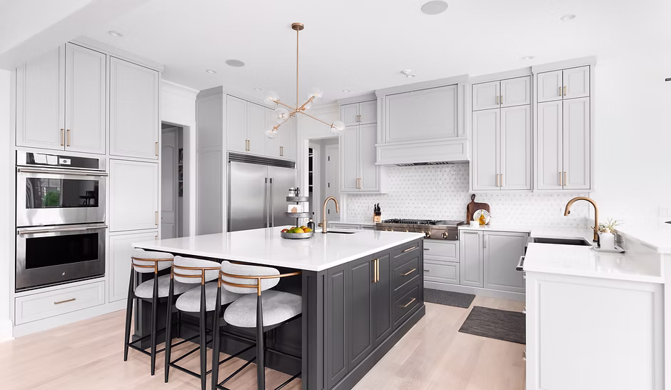 Modern kitchen with white cabinetry, a large black island, stainless steel appliances, and gold accents. Perfect inspiration for your next Pensacola remodeling or kitchen remodel—bright, minimalist decor and a stunning pendant light complete the space.