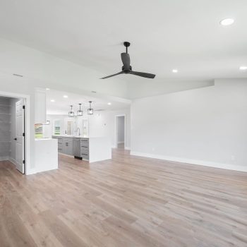Spacious, modern open-concept living area with light wood floors, white walls, recessed lighting, ceiling fan, visible kitchen with pendant lights, and a walk-in pantry—ideal for your next Pensacola remodeling or kitchen remodel project. Large and bright.